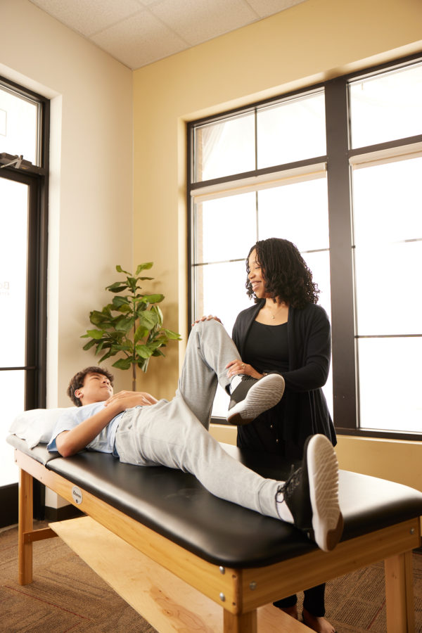 female physical therapist stretching teenage boys left leg and knee