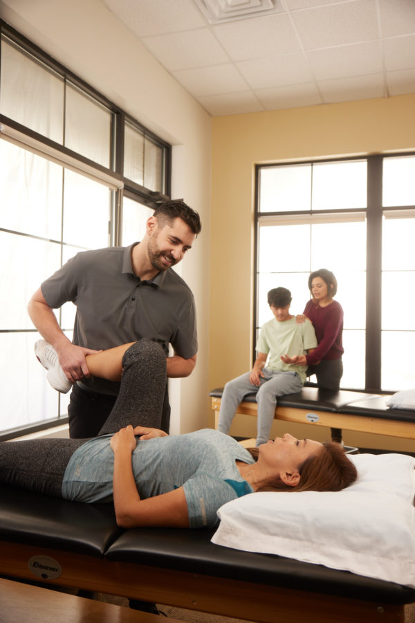 young male physical therapist stretching out his female patients knee and legs