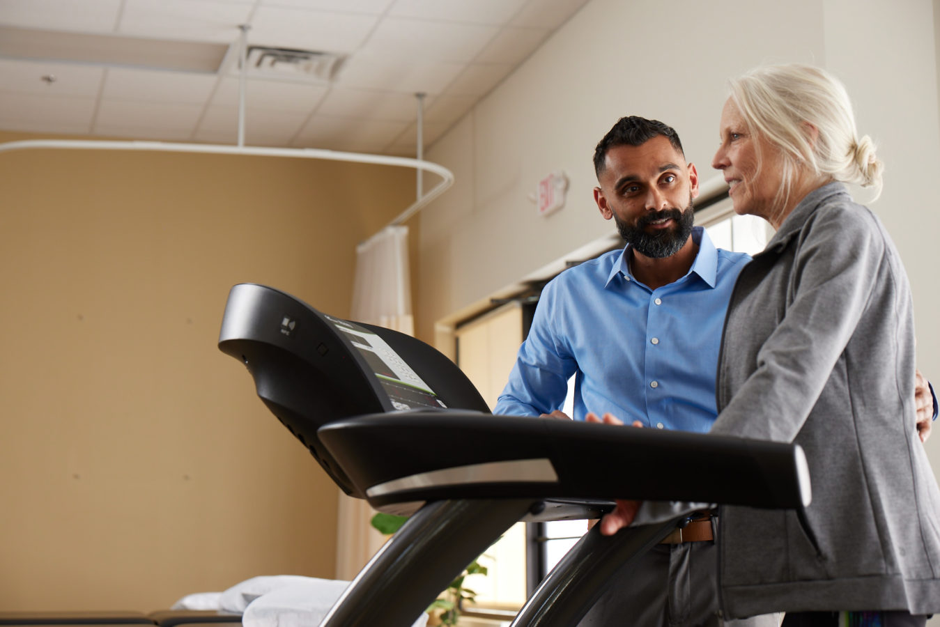 older woman walking on a treadmill with male physical therapist standing next to her