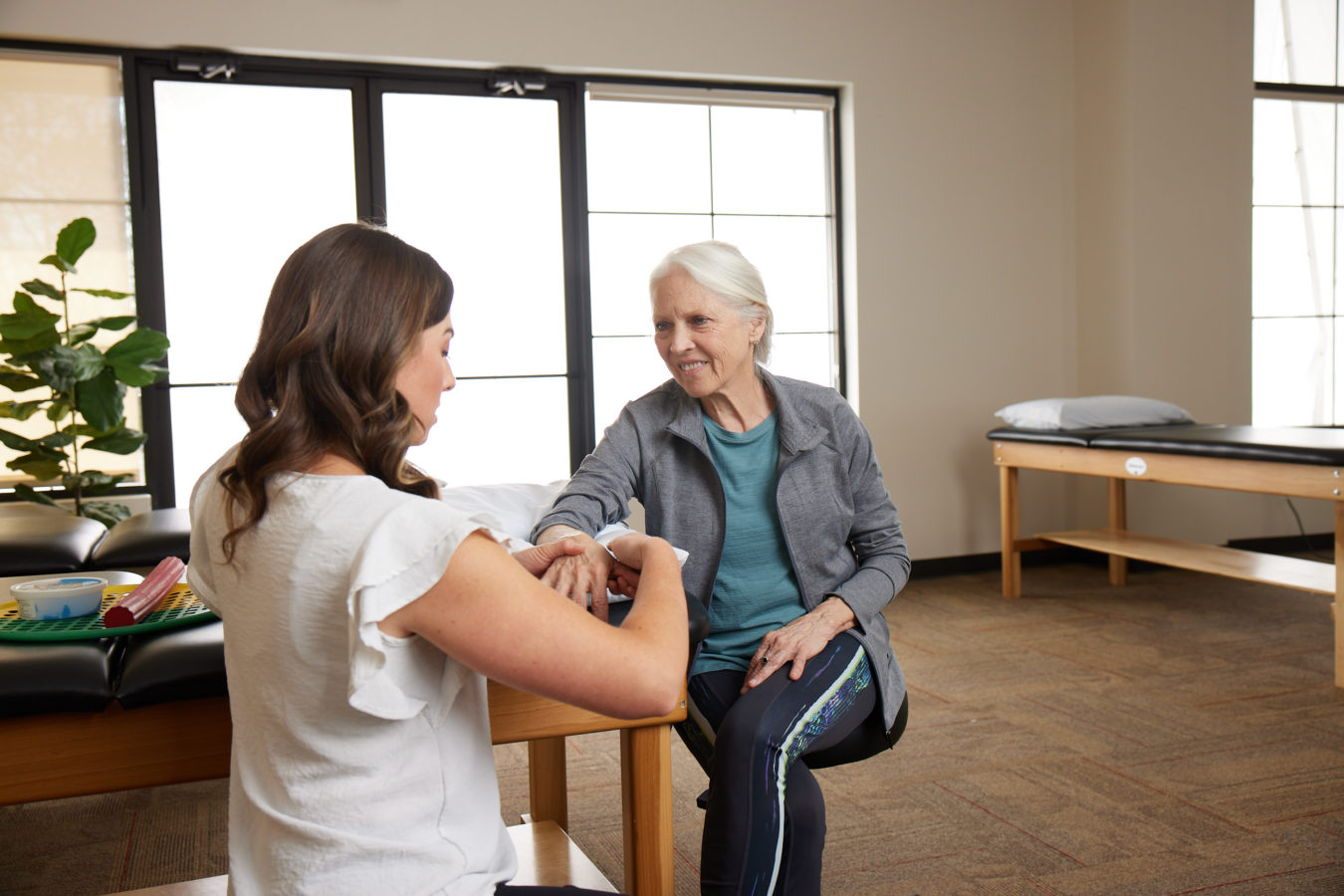 older woman getting her hand examined by female physical therapist