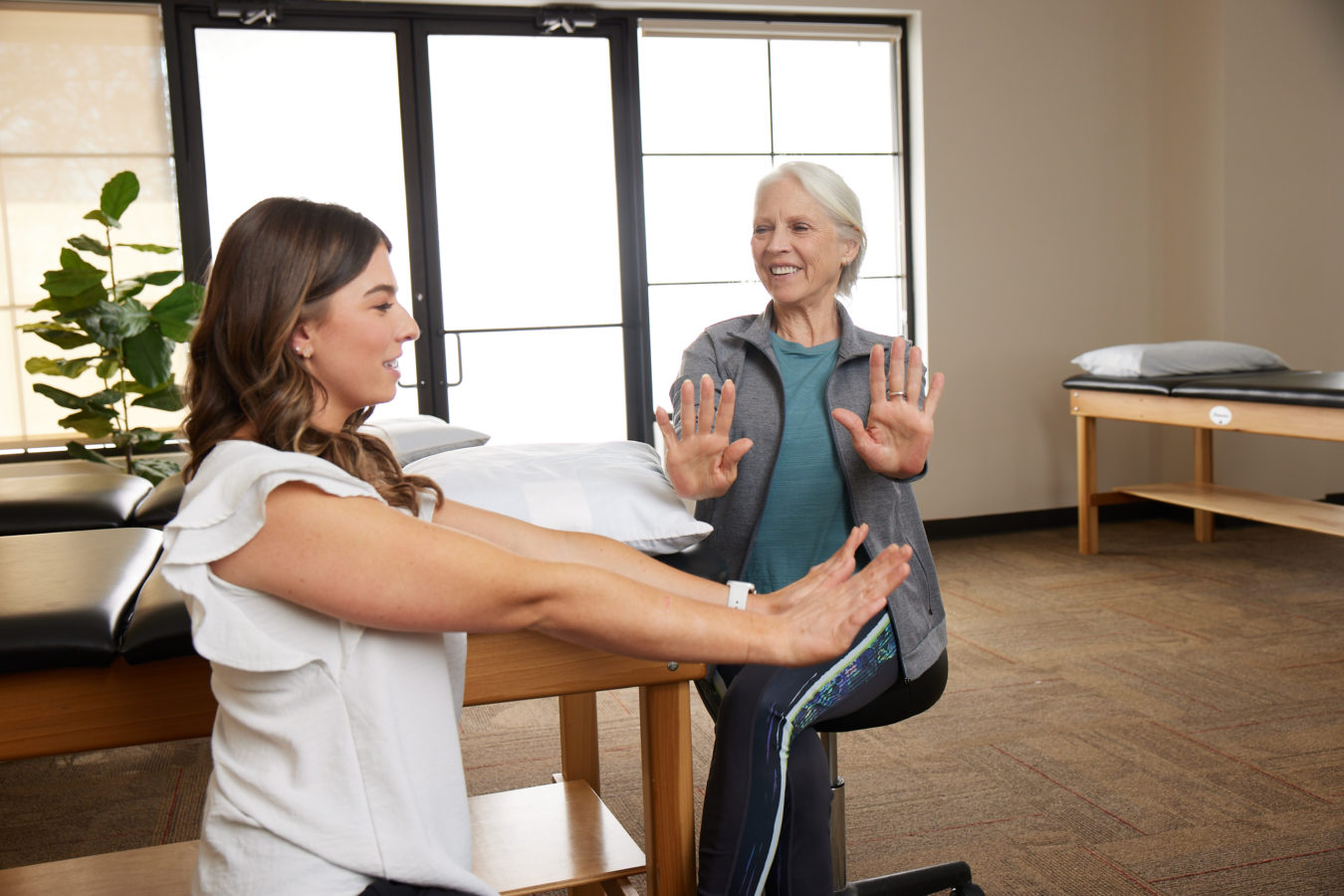 female physical therapist showing older woman how to lift arms