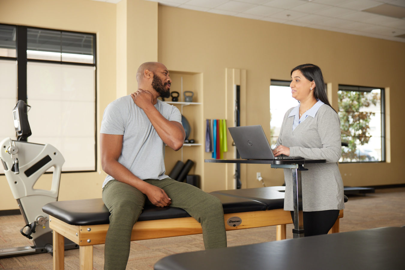 male patient sitting down speaking with his female physical therapist
