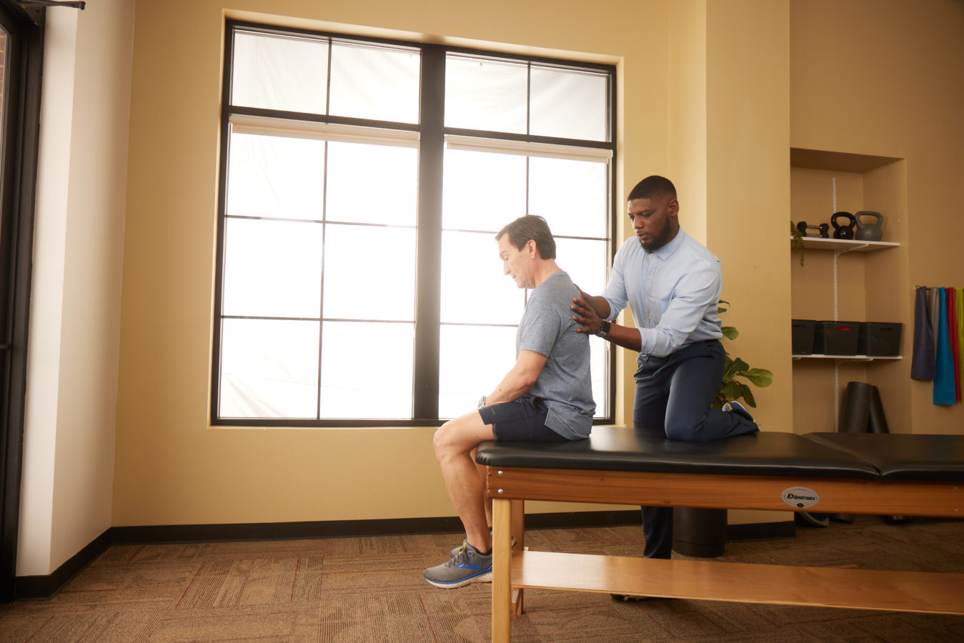 young male physical therapist helping male patient with back pain