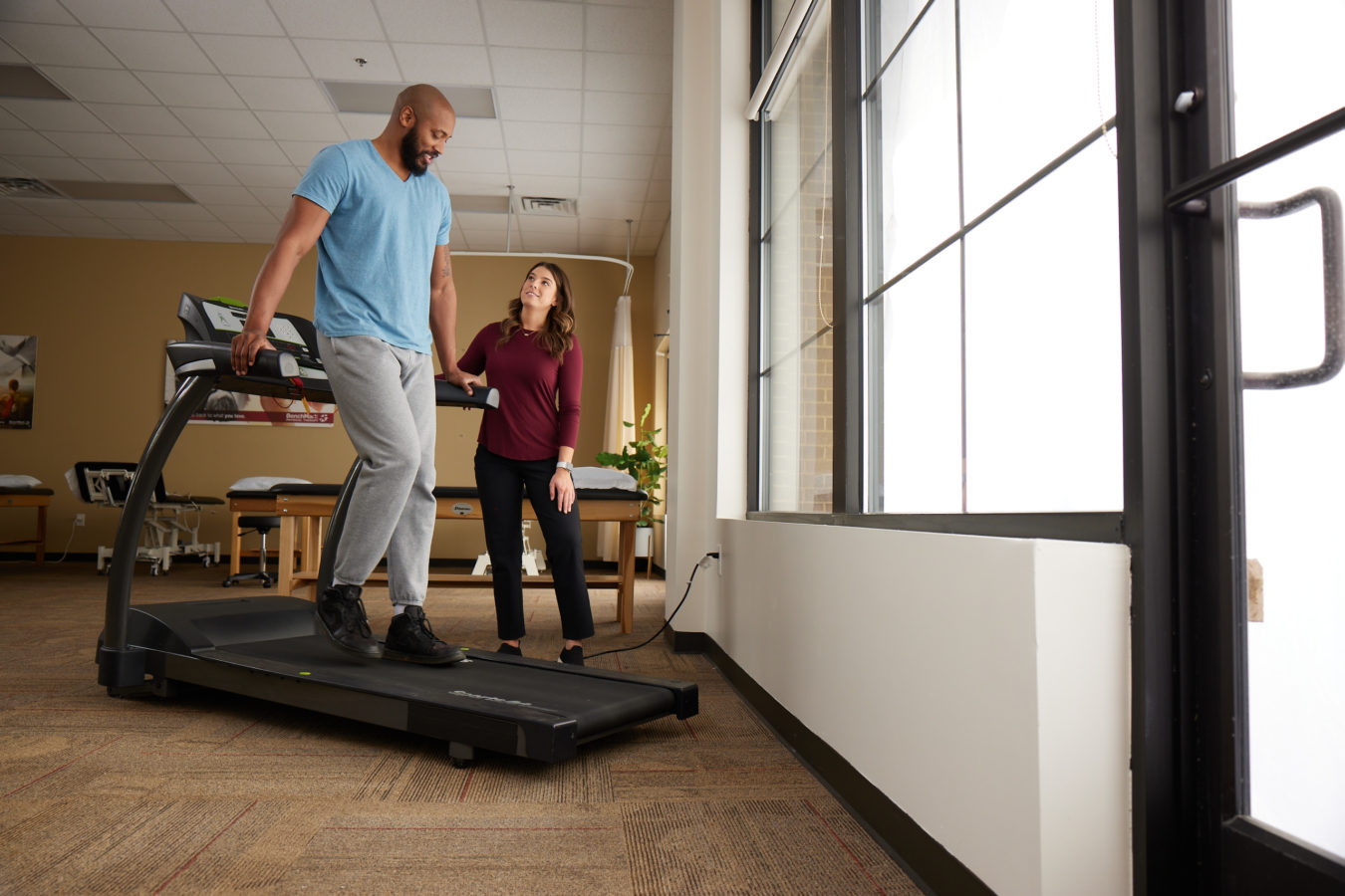 fit man walking backwards on a treadmill while female physical therapist watches him