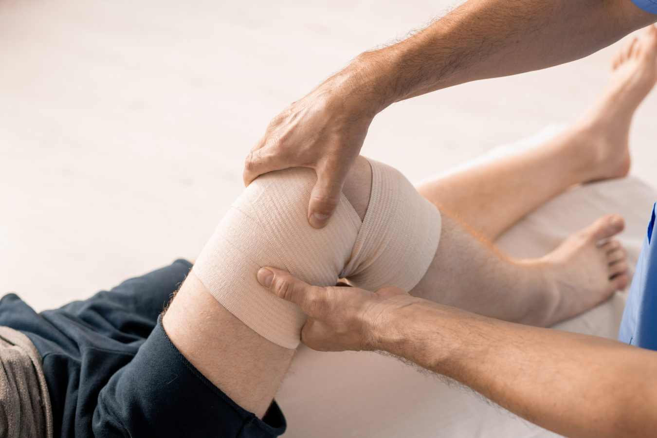 Hands of male clinician wrapping knee of disable patient with flexible bandage