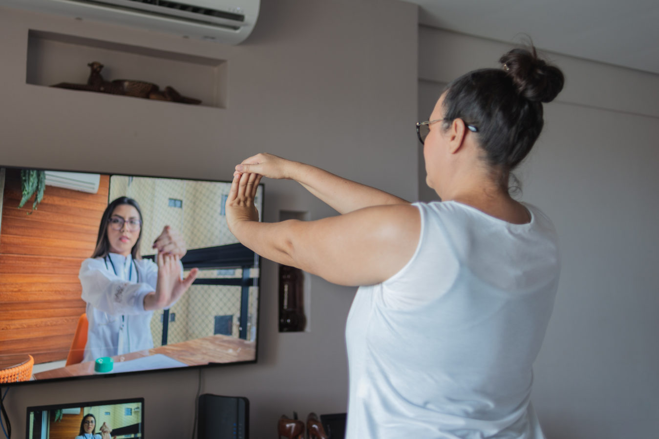 Mature woman watching and copying wrist exercises at home, guided by a virtual physical therapist