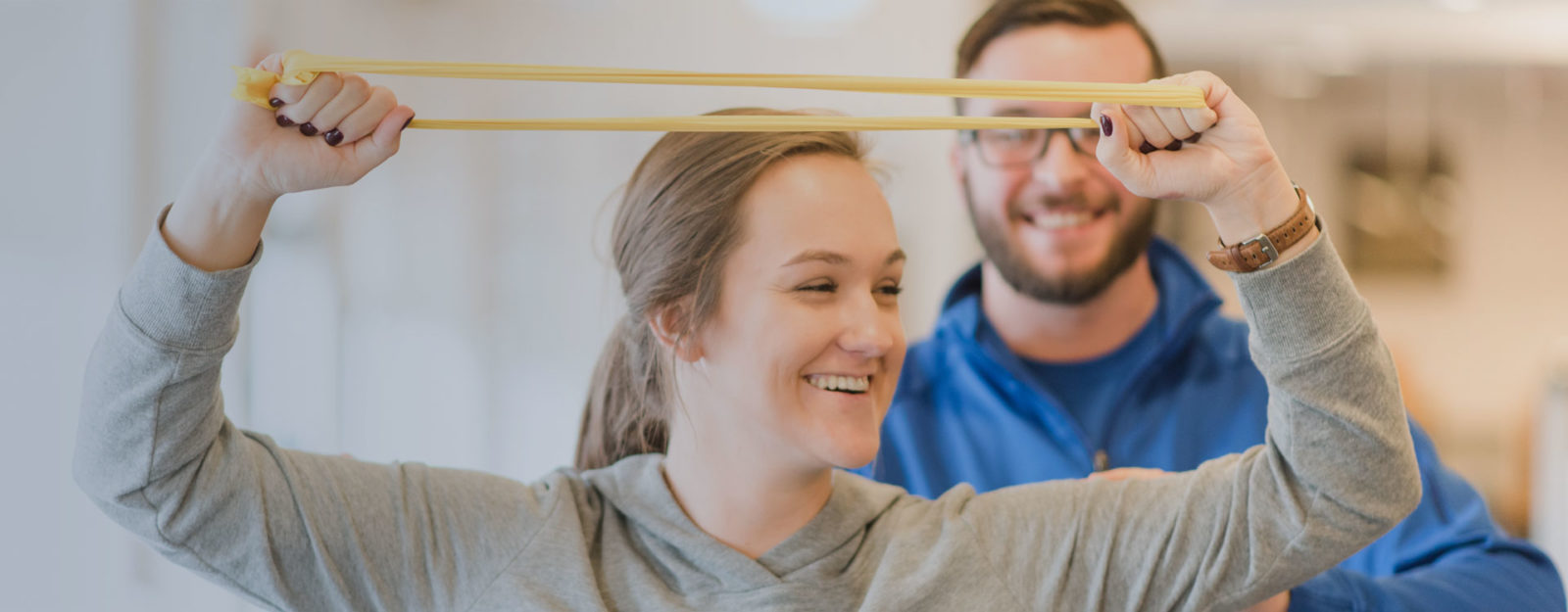 young energetic woman holding an exercise band with male physical therapist standing behind her