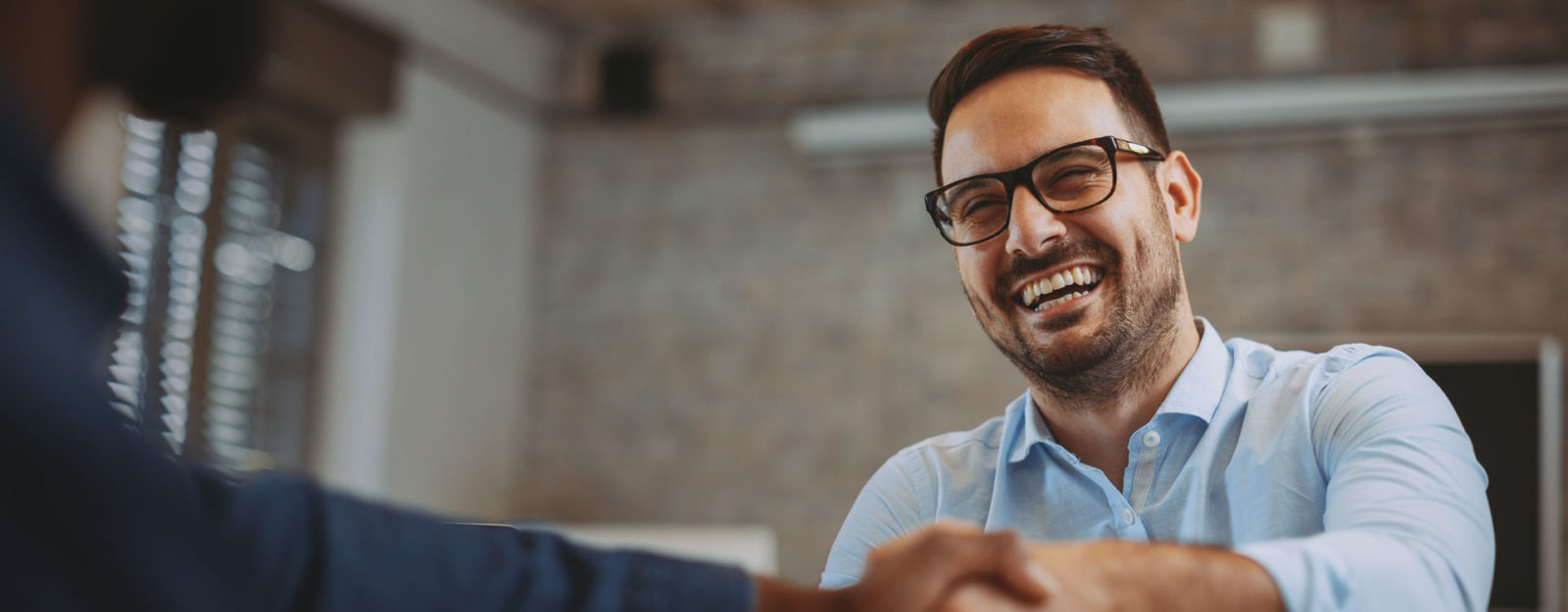 smiling man with glasses shaking hands with someone else