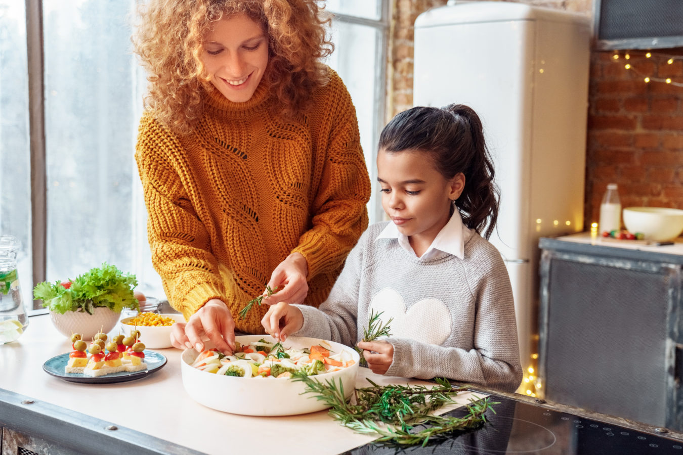 Happy curly woman and mulatto girl niece making healthy vegan food for family feasting