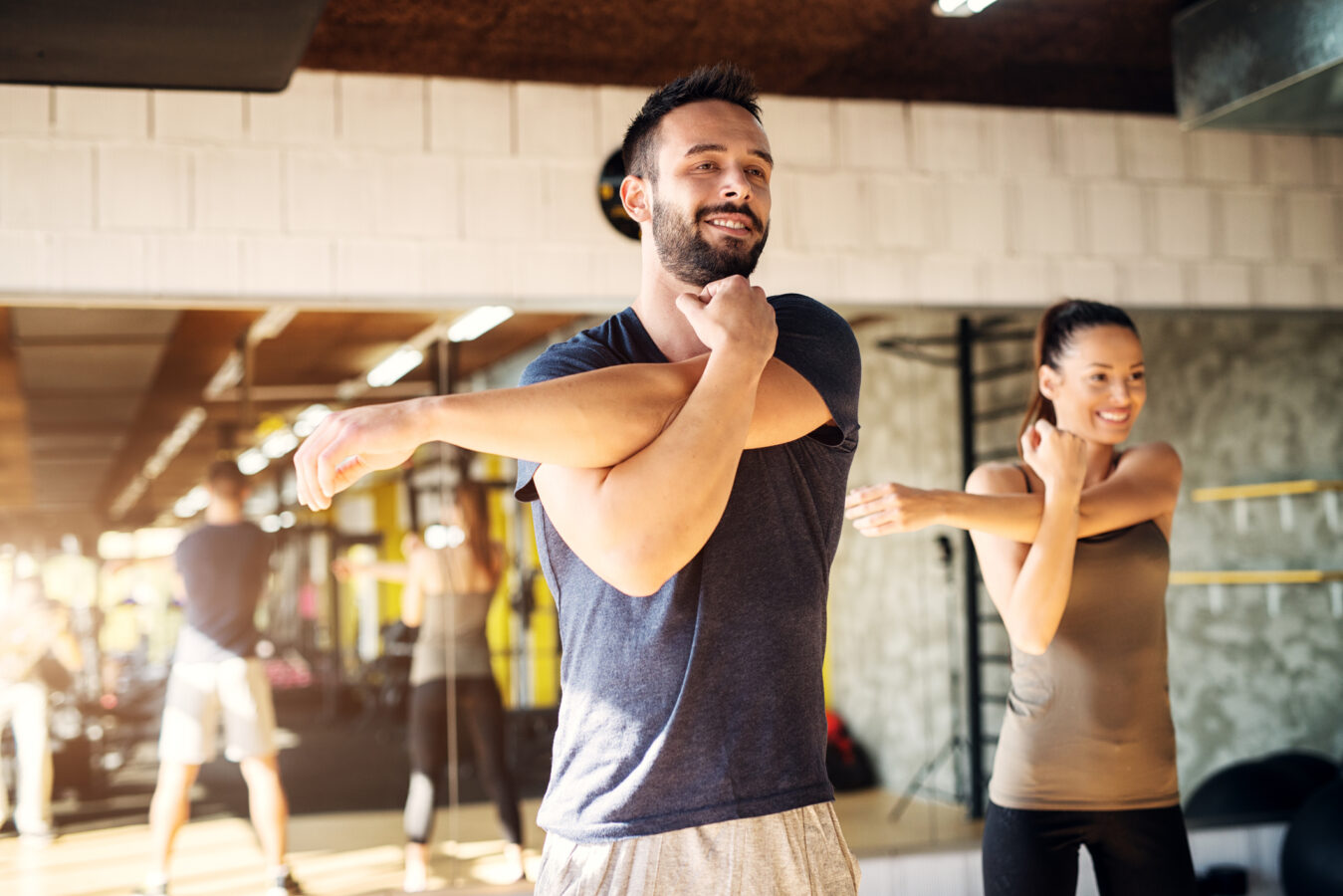 Strong young smiling athletes stretching shoulder in a gym .